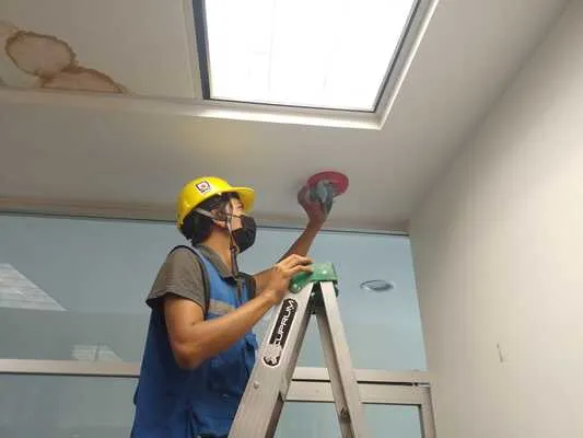 Personal de seguridad industrial limpiando un sensor de humo integrado al sistema de alarma contra incendio en oficina.
