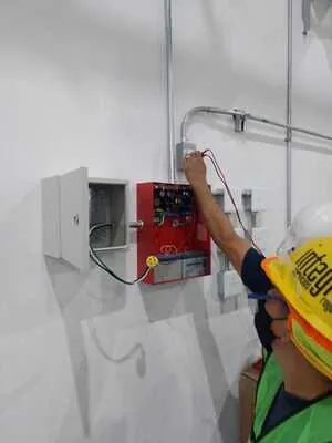 Ajuste y limpieza de una estación manual de jalón para activación de alarma contra incendio en un pasillo industrial.